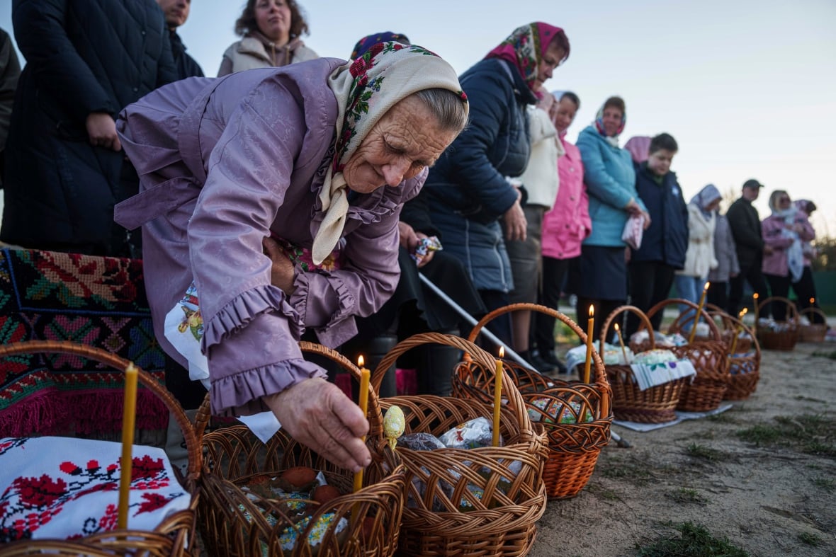 An elderly woman places a candle in an Easter basket.