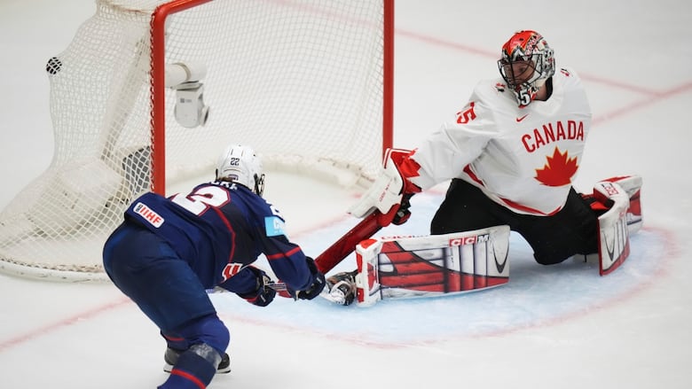 A female ice hockey player shoots the puck past an outstretched goaltender.
