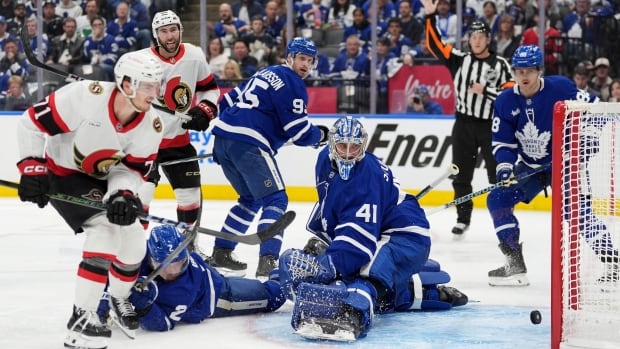 Ottawa Senators' Ridly Greig (71) scores a goal on Toronto Maple Leafs' goaltender Anthony Stolarz (41) as Simon Benoit (2) tries to defend during third period NHL playoff action in Toronto, on Sunday, April 20, 2025. A group of men in hockey gear are around a net as the puck goes in.