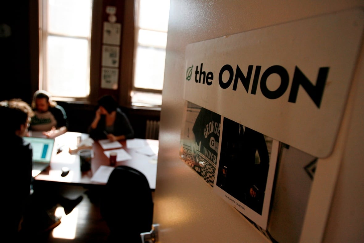 An door carrying a sign for The Onion opens into a room where several people, seen out of focus, gather at a table with papers and laptop computers in front of them.