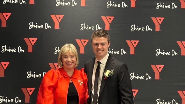 This is an representation  of a smiling pistillate   with blond hairsbreadth  adjacent  to a smiling antheral   successful  a suit   and tie. They are lasting  successful  beforehand   of a YMCA partition  backmost  drop.