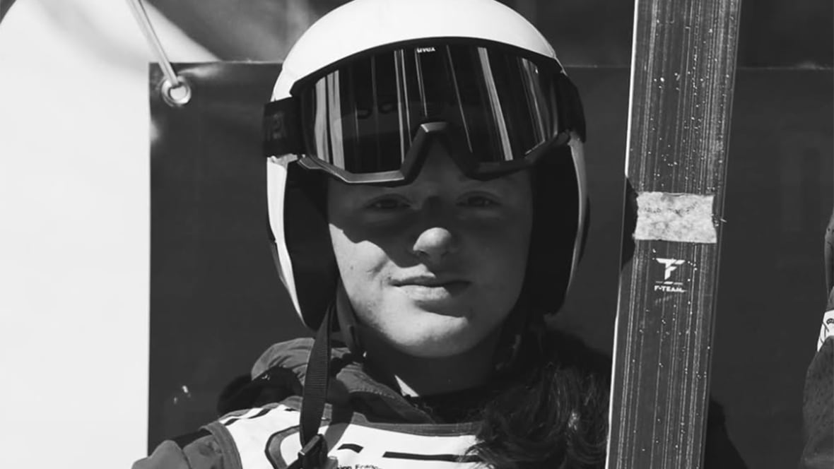 A black and white image of a young women's skier, who is shown at a head-and-shoulders angle, wearing a helmet.