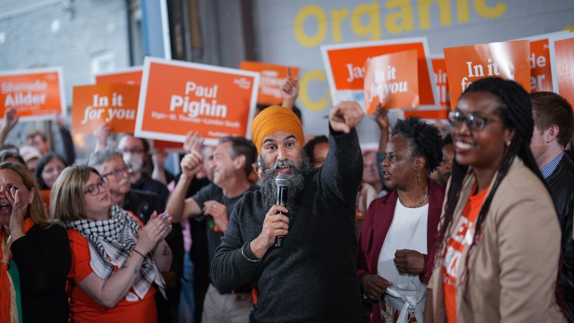 Jagmeet Singh, surrounded by a radical  of his supporters, holds a microphone successful  1  manus  and points guardant  with his right. 