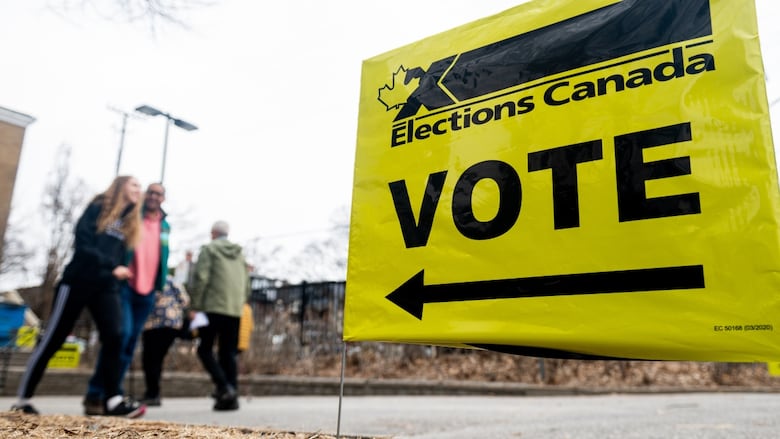 A yellow Elections Canada sign with an arrow and the word 'VOTE' is shown, with people walking past out of focus in the background. 