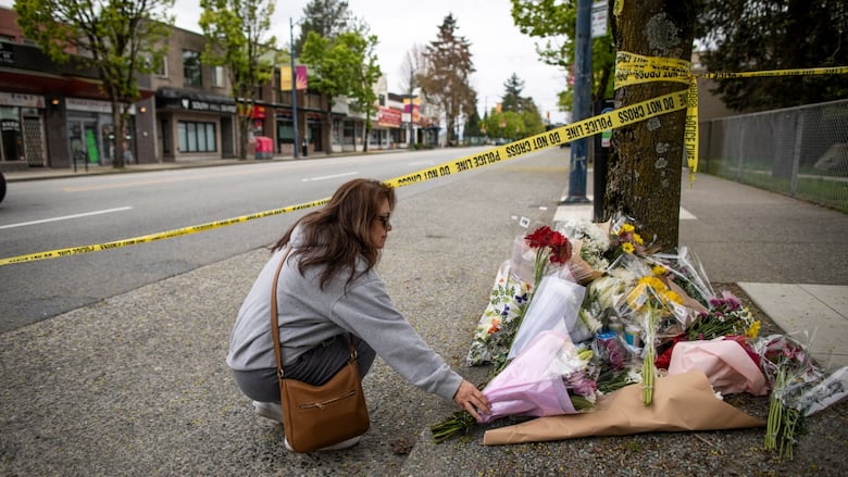 A woman kneels down to set a bouquet of flowers next to a lamp post.