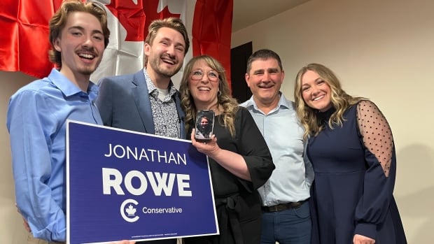 A smiling family hold a sign for the Conservative candidate, Jonathan Rowe.