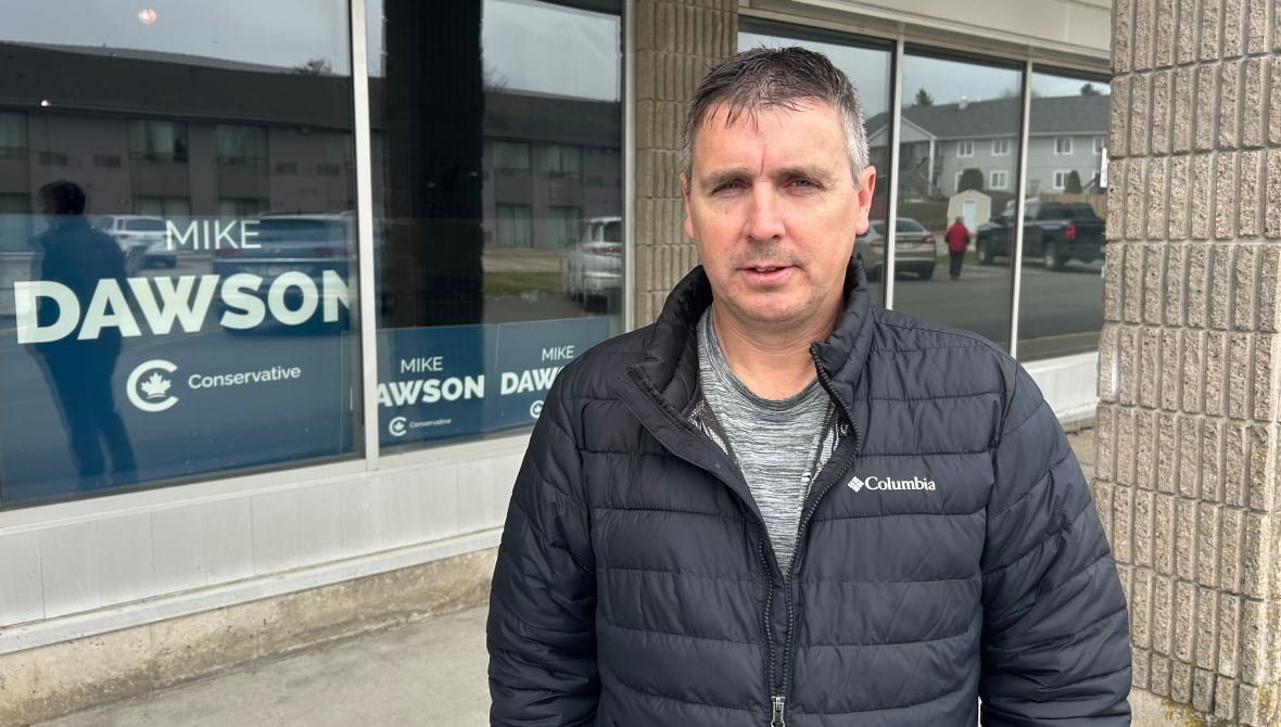 A man in a jacket standing in front of a Dawson campaign sign