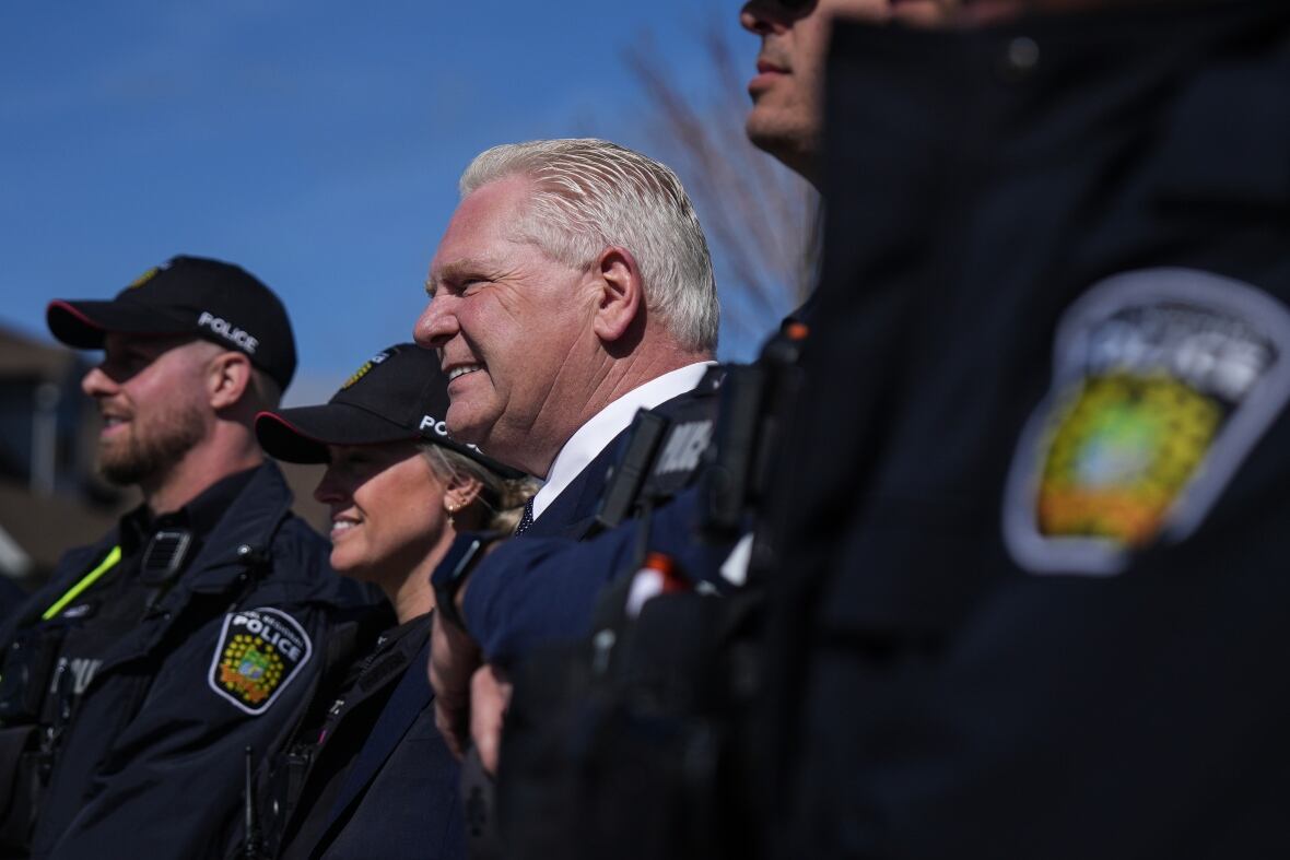 A antheral   smiles portion    flanked by constabulary  officers.