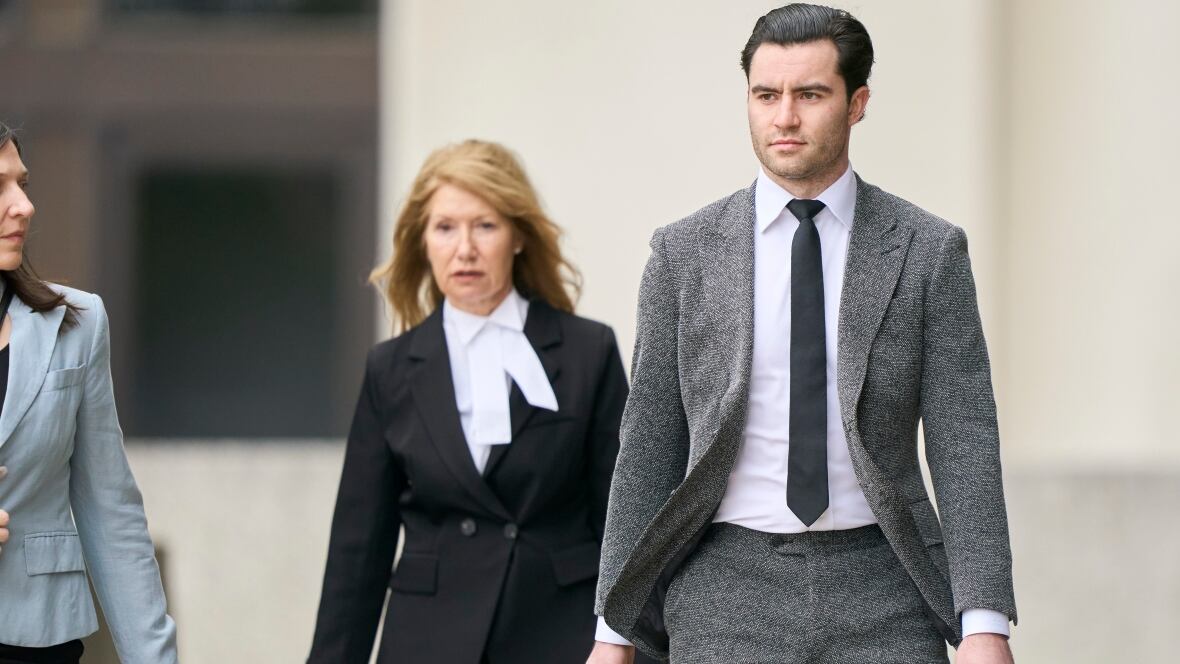 Un hombre con traje gris camina junto a dos mujeres vestidas formalmente.