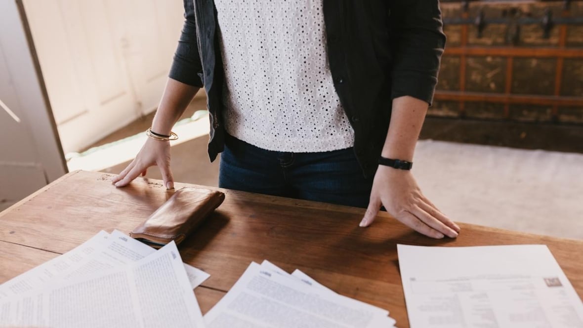 A person standing at a wooden desk with a lot of paperwork spread over it.