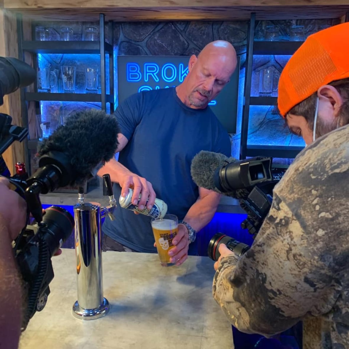 Wrestler (Stone Cold) Steve Austin is shown pouring a beer, portion    a filmmaker wearing a reddish  chapeau  films him.