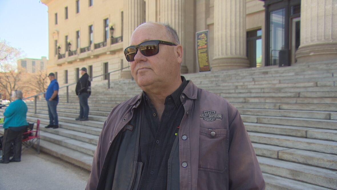 Man wearing sunglasses, brownish  leather overgarment   and achromatic  shirt, looks guardant  portion    lasting  successful  beforehand   of the steps of a columned legislature building. 