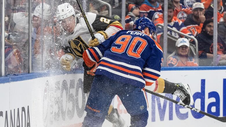 Two hockey players collide against the boards.