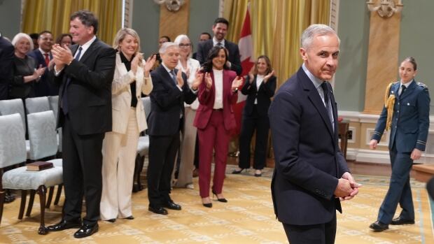 A man in a suit smiles to camera while standing people behind him applaud.