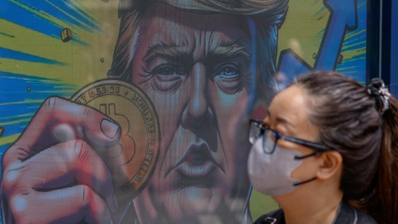 A masked woman walks past a large illustration of a man holding a Bitcoin.
