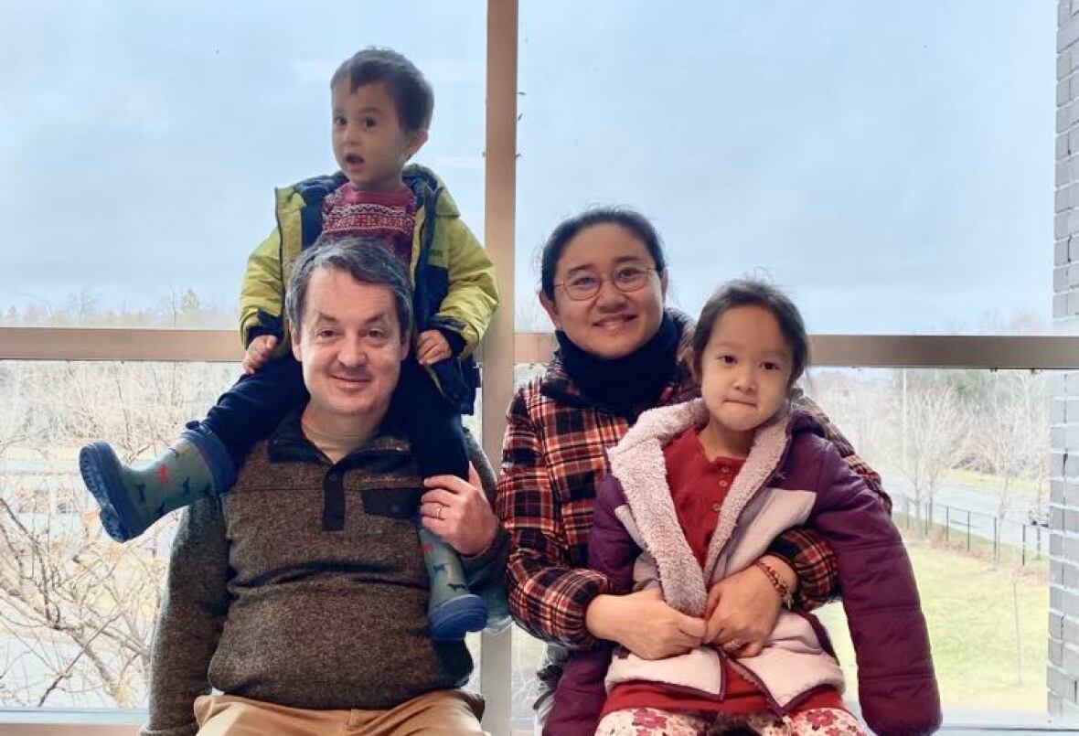 A family of four sits casually in front of a window
