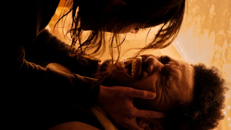 A man lying on his back grimaces in what appears to be pain. A woman is lying on top of him, and holding his head in her hands. 