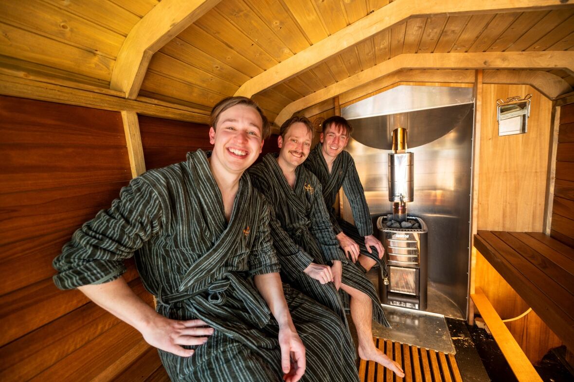Three smiling men in robes in a sauna