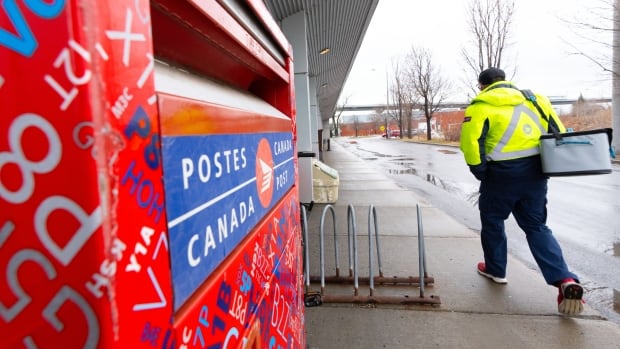 A postal worker walks past a post box.