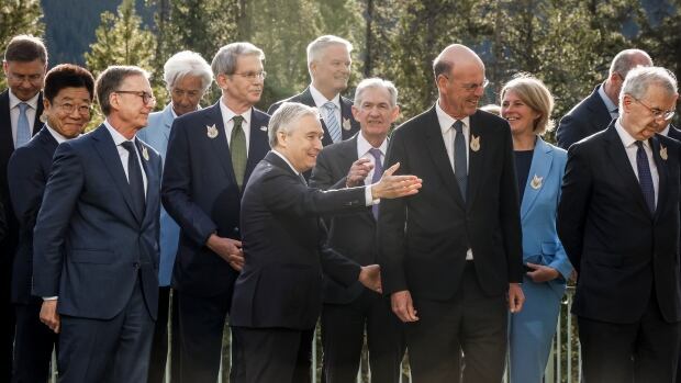 Canada's Finance Minister Francois-Philippe Champagne, centre, directs his colleagues to the meeting room following a family photo with colleagues at the G7 Finance Ministers meeting in Banff, Alta., on May 21, 2025. about a dozen suit wearing officials stand for a photo outside with trees behind them