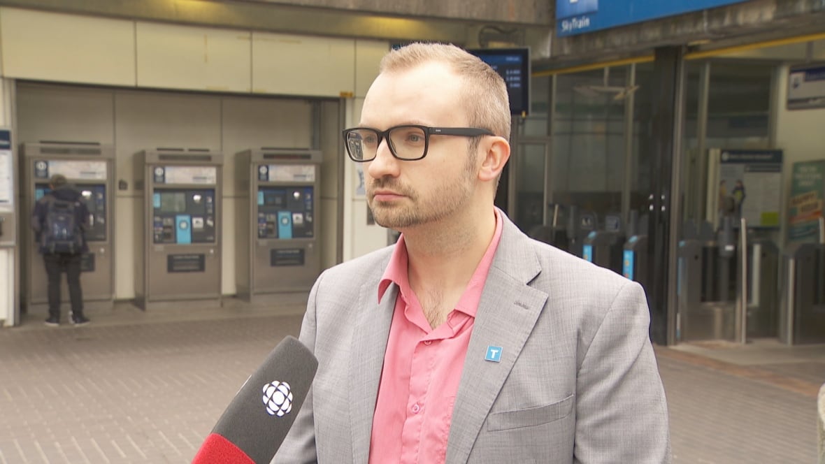 A antheral   wearing a brace  of glasses and dressed successful  formals talking is lasting  extracurricular  a SkyTrain presumption    during a tv   interview. 