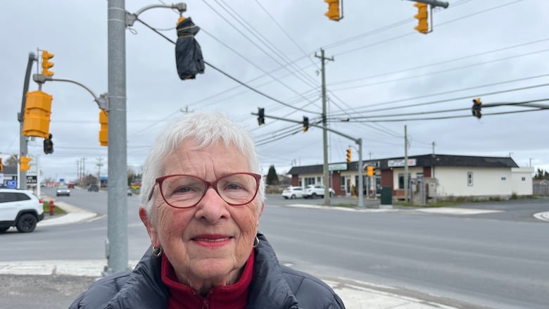 A woman stands in front of an inactive set of street lights at a busy intersection in Bay Roberts.