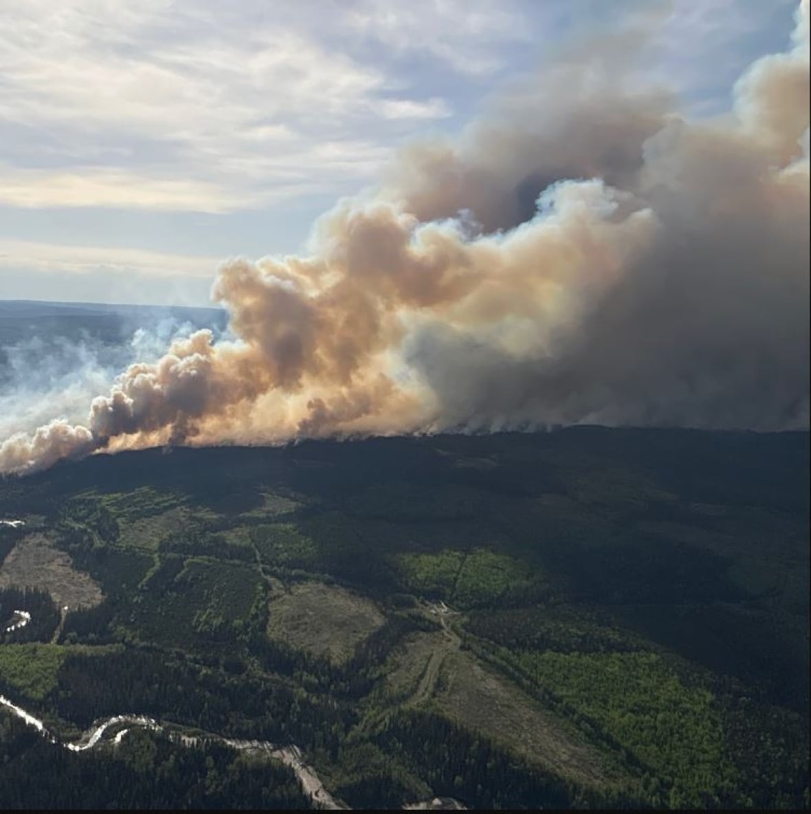 A aerial view of a wildfire in the forest. Smoke billows over the skyline. 