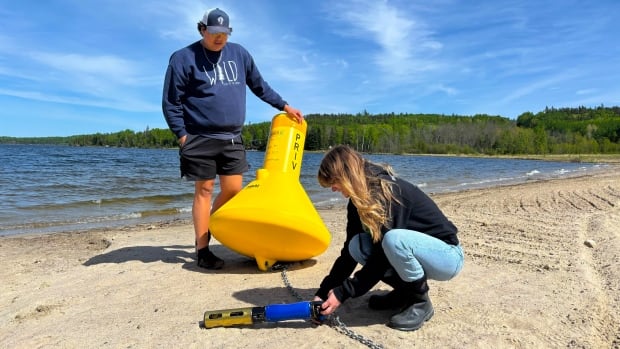 Two people are seen on a beach with a bright yellow buoy and a cylindrical device.