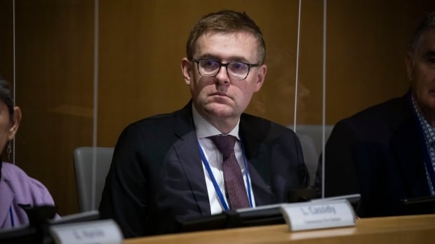 A white man with glasses looks to his right at a board meeting.