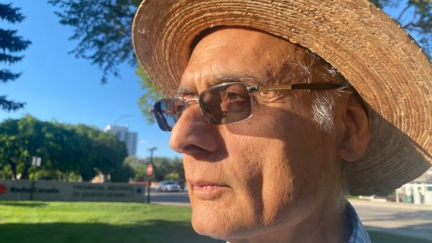 A South Asian man wearing tinted glasses and a straw hat looks into the distance.