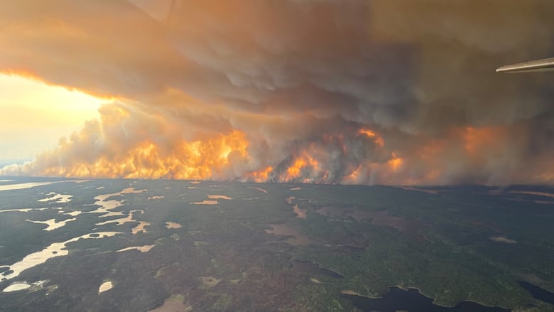 A plume of fume  billows to the entity  from a wildfire adjacent   lakes and forest.