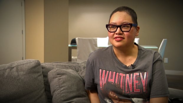 A woman with short hair and glasses sits on a couch with a Whitney Houston T-shirt on.