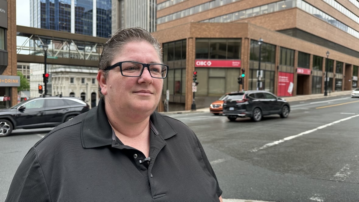 A woman stands next to an intersection with cars and buildings in the background.