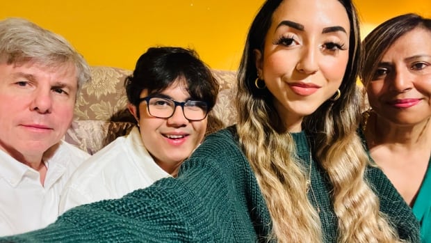 Ishaan Holloway (second from left) poses with his parents & sister. Holloway is profoundly autistic, with limited speech and about to graduate highschool. Four people sit together on a couch smiling while one of them takes a selfie.