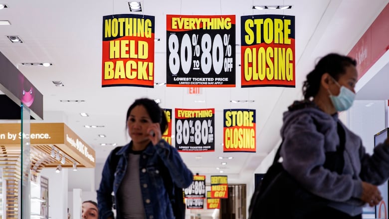 Two people walk in a store with signs reading 'Everything 80% off', 'Store closing', and 'Nothing held back!'