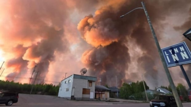 Pink and grey smoke in the sky above a street.
