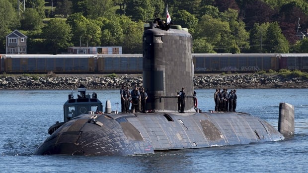 A submarine at the surface of a body of water with people standing on top.
