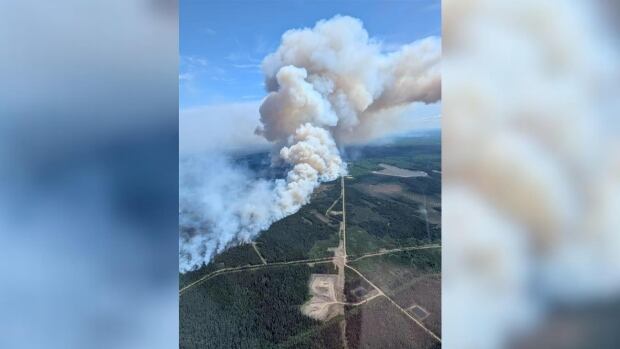 Plumes of smoke rise from a wildfire near a forested highway.