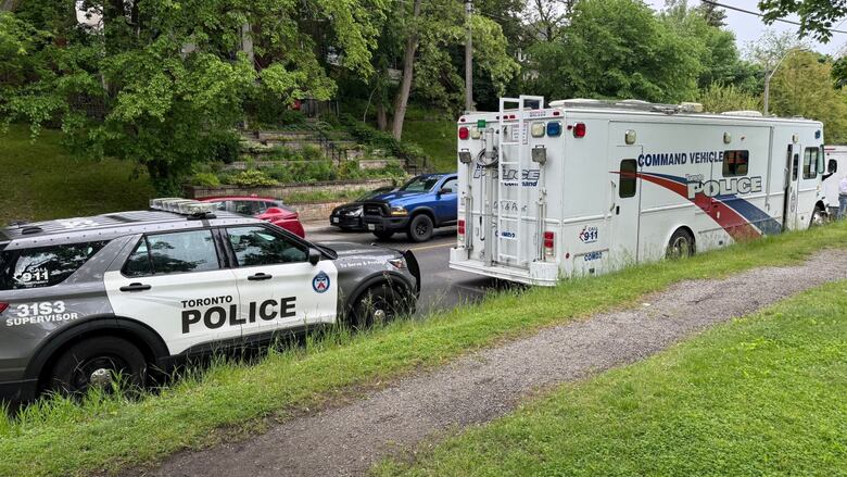 A Toronto police SUV and command vehicle are parked on a city street next to High Park on a grey, wet spring day