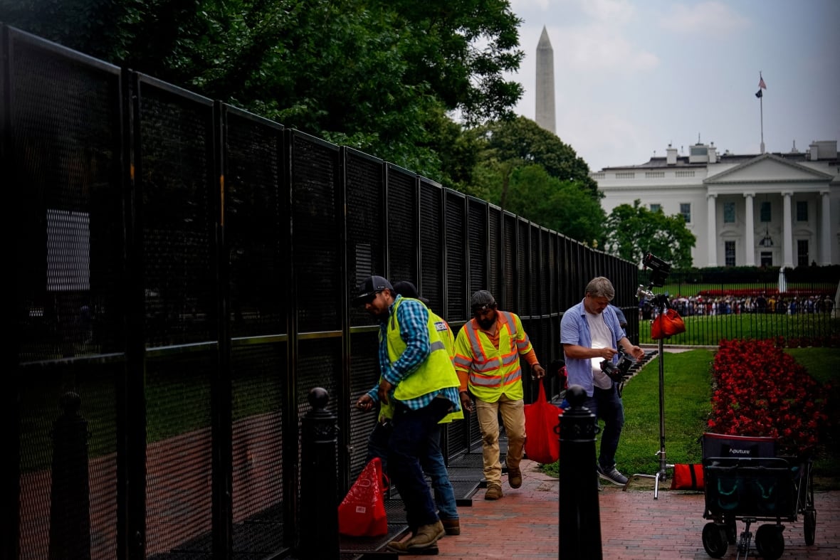 Half a dozen people working near tall security fencing erected around the White House.