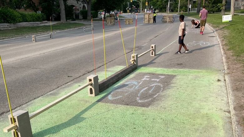 A handpainted bike lane is flanked by concrete blocks and posts.