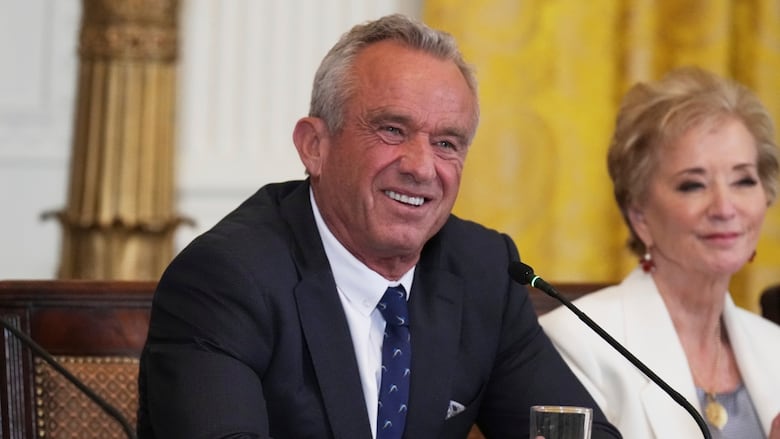 A man smiles, sitting behind a microphone.