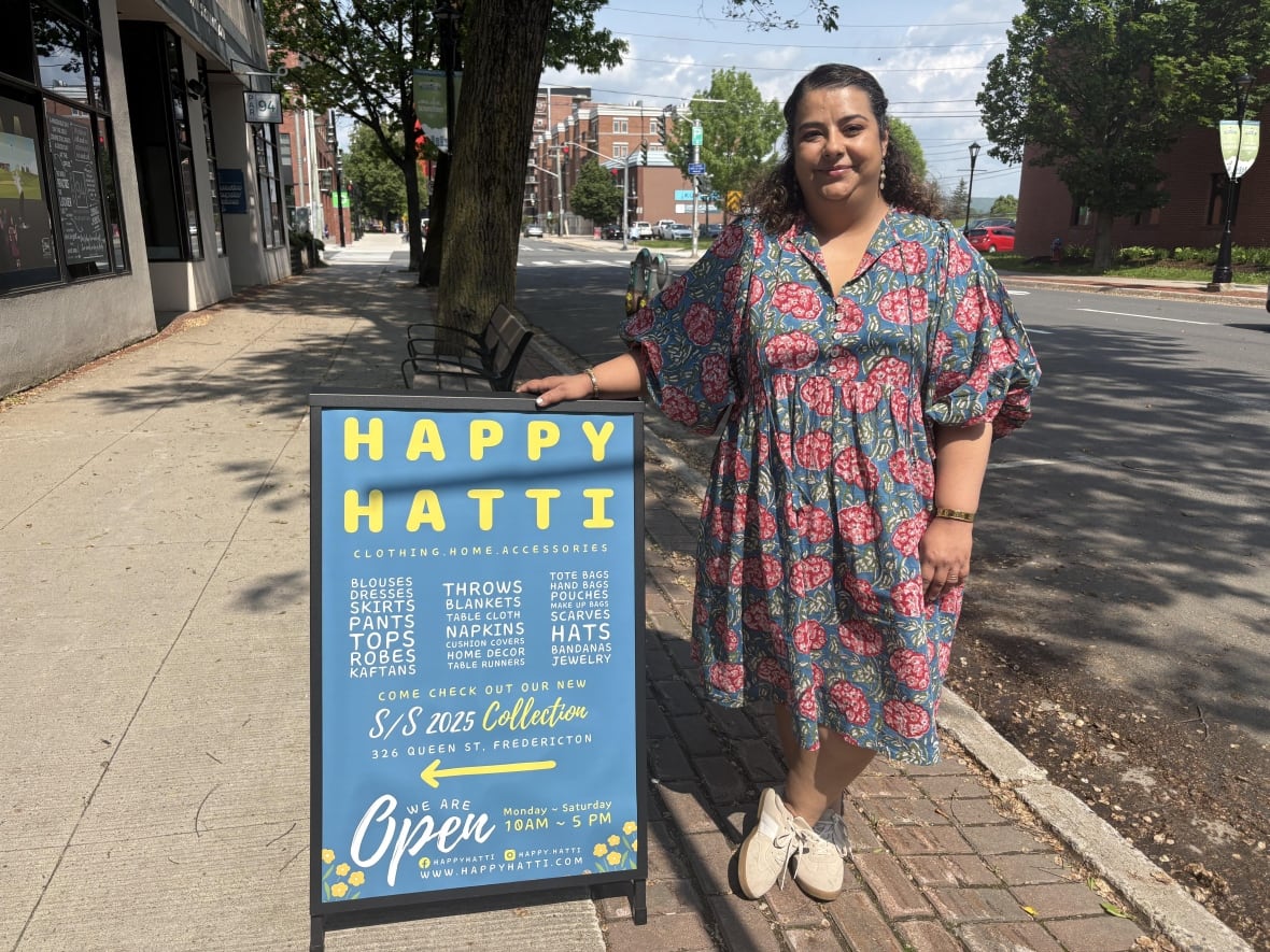 Woman in blue dress with mid-forearm sleeves and a pink flowers design posses next a blue sign. 
