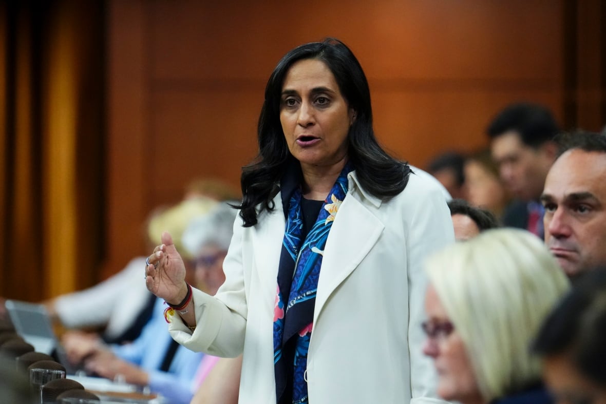 A woman with black hair wears a white coat standing at the house