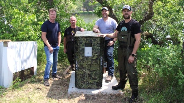 Four men stand by a large camo colour box.