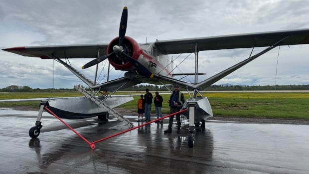 A group of people pose under a plane.