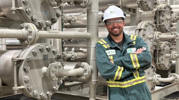 Clayten Wenass stands in front of pipes wearing a hard hat and safety glasses