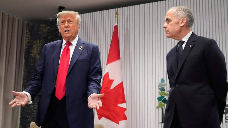 Two men wearing suits stand side by side, one man is talking, the other is looking at him
