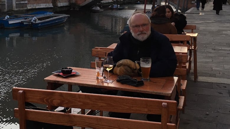 A man sitting at a wooden table alongside a canal in Italy.