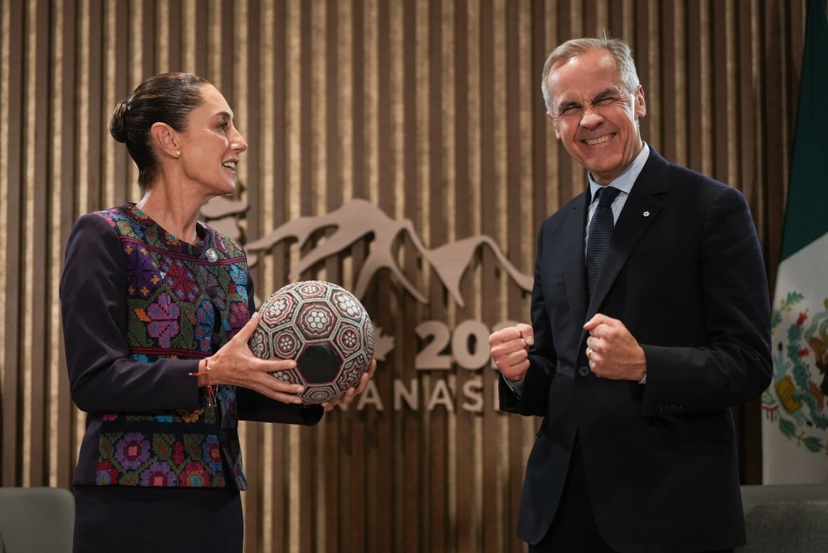 A woman with a colourful vest offers a man in a suit an artful soccer ball.